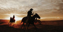 Silhouettes of cowboys on horseback against a sunset sky.