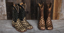 Two pairs of western cowboy boots displayed side by side. The left pair features a black shaft with white embroidered stitching and a gold-toned scaled lower body.