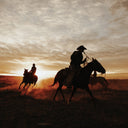 Silhouettes of cowboys riding horses against a sunset sky.