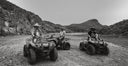 Three people on ATVs in a desert landscape with mountains in the background