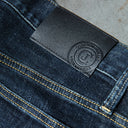 Close-up of dark blue denim jeans showing a black leather patch with an embossed circular logo that reads 'Cody James Brand Western Wear.'